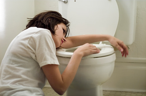 Sick young woman leaning on toilet bowl